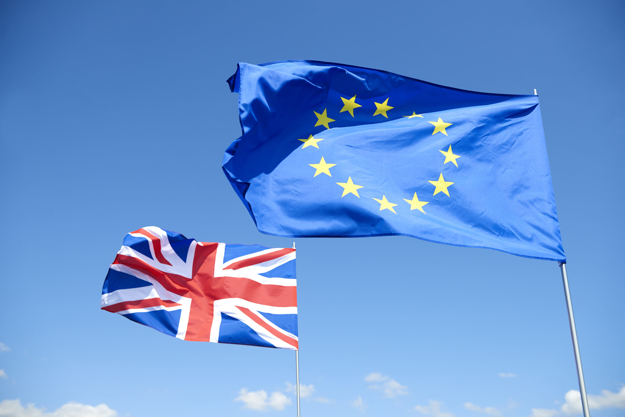 UK & EU Flags blowing in the wind in front of blue sky.