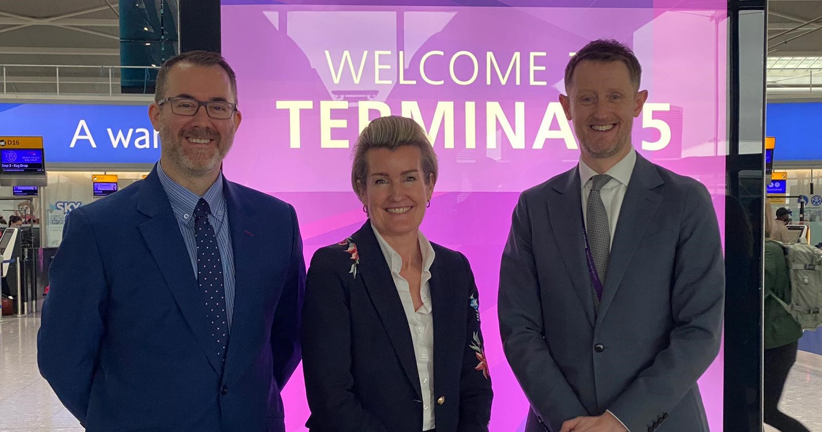 Craig Beaumont, Chief of External Affairs at the Federation of Small Businesses, Shevaun Haviland, Director General of the British Chambers of Commerce, and Dale Reeson, Director of Operations at Heathrow Airport. Stand side by side in front of pic neon display board at Heathrow's Terminal 5.
