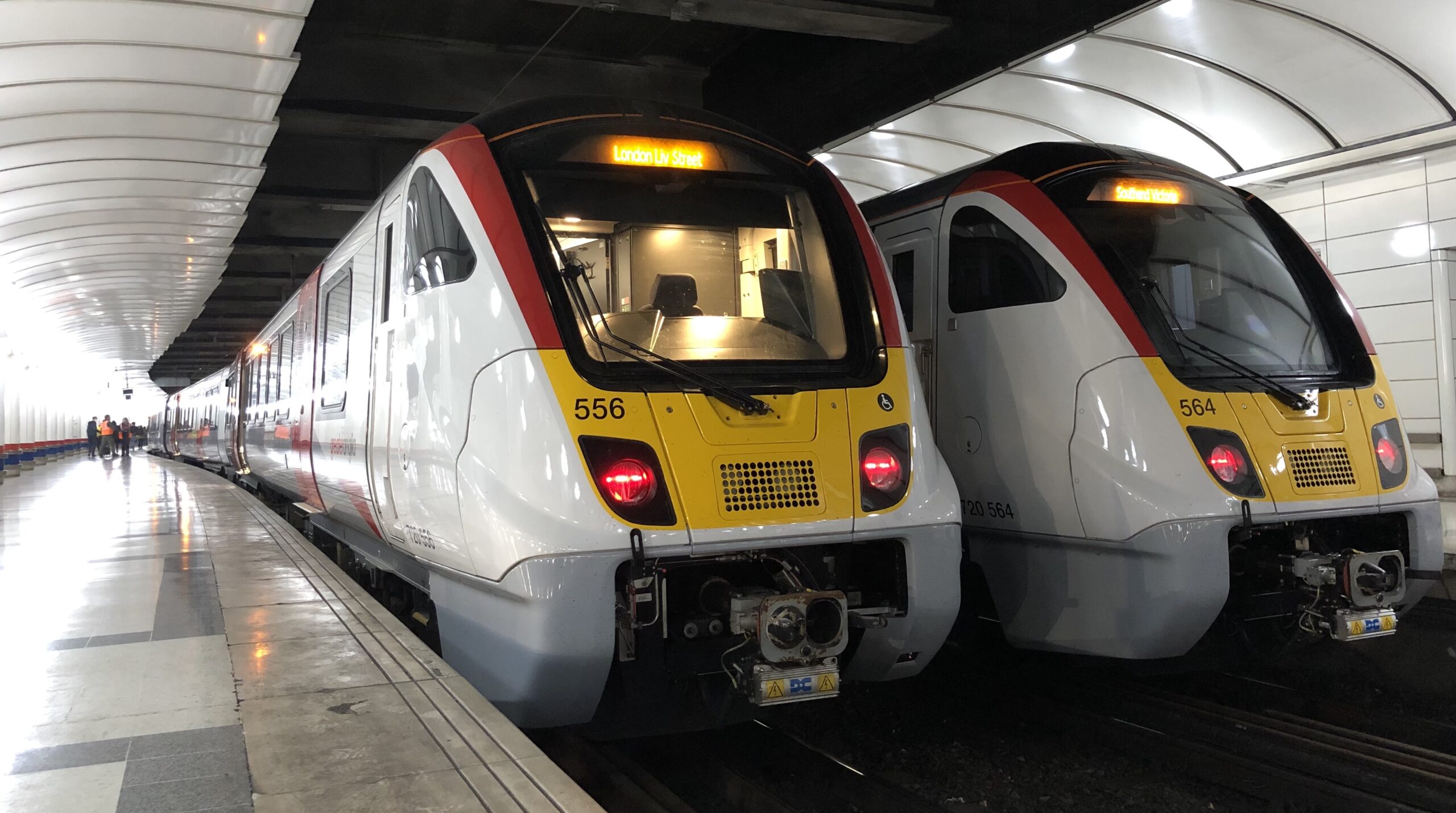 Two Greater Anglia trains positioned side by side pulled into a train station with platforms either side.