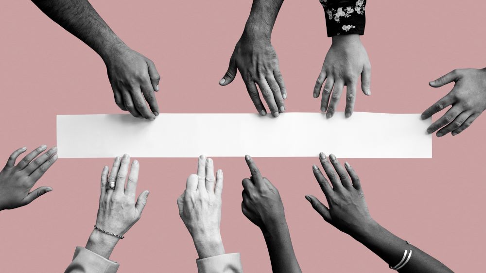 Diverse hands from a range of ethnicity, genders and ages reach towards a long rectangle strip of white paper on pink background.
